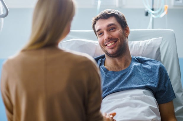 smiling man in hospital bed talking to visitor