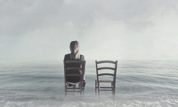 two chairs in water at the beach, only one occupied and that is a woman