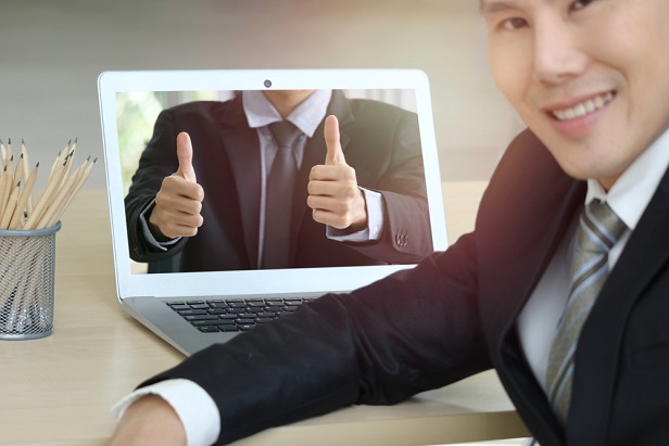 man at laptop with colleague online giving a thumbs up