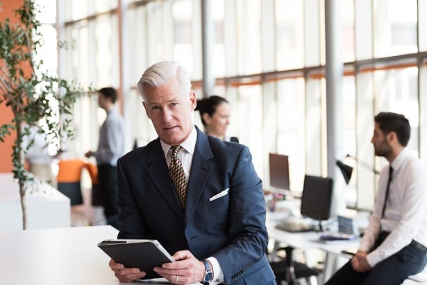 Older business man with tablet and team behind him