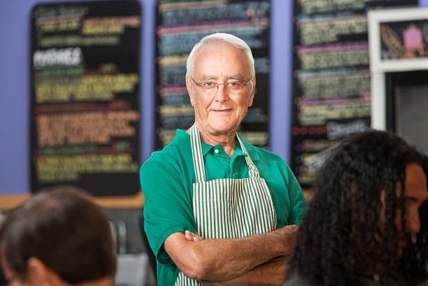 older man wearing butcher's apron smiling at camera