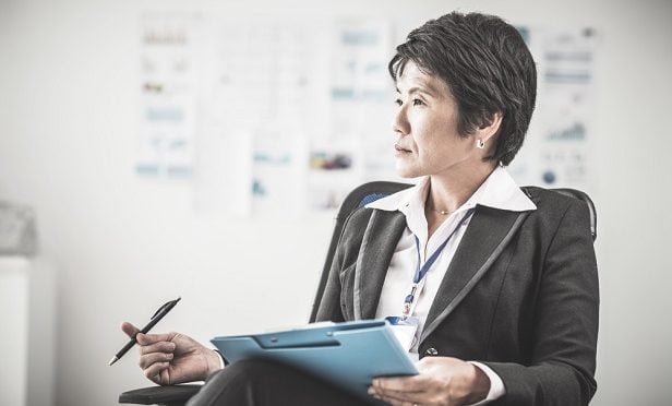 female executive in chair with pencil and notes looking in distance and thinking