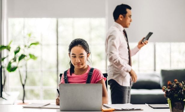 girl online on laptop with dad in background on phone