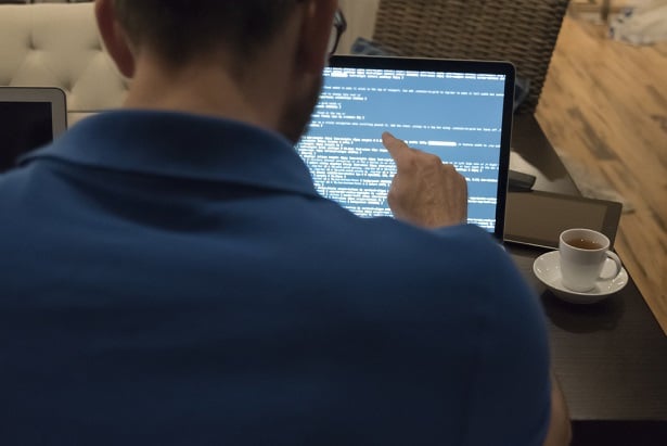 male white IT pro in a blue polo shirt at screen looking at lines of code
