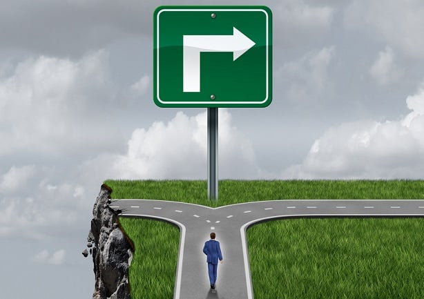 person standing at fork in road, half of road is gone, other half has an arrow