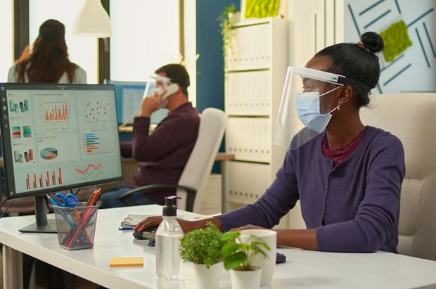 woman at desk wearing mask and face shield in office