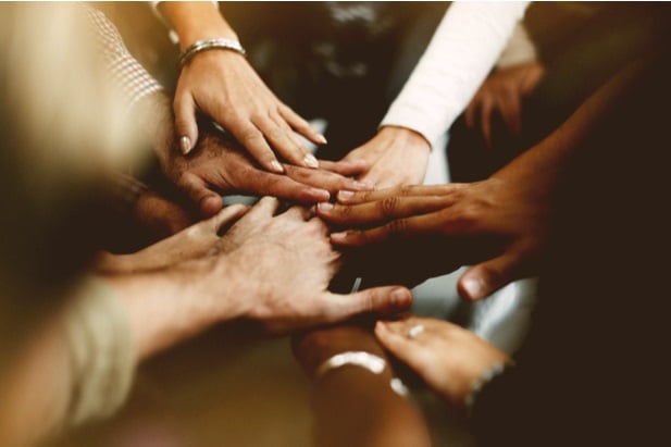 people's hands on top of hands in a gesture of unity