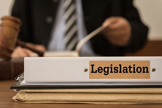 closeup of business suited man in tie with sign at table saying Legislation