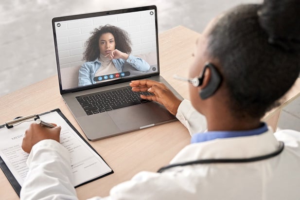 female doctor or nurse in white lab coat speaking on computer to woman