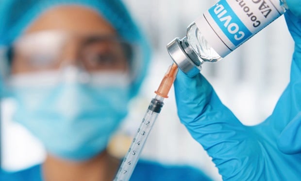 Close up shot of young female healthcare specialist hands holding ampoule with coronavirus vaccine preparing injection for covid vaccination, doctor or nurse in protective uniform work with vaccine