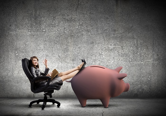 Woman relaxing with her feet on a giant piggy bank. (Photo: Shutterstock)