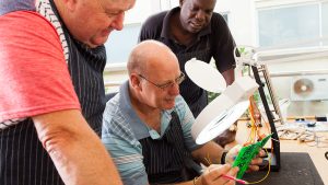 Group of men in work clothes examining circuit board.
