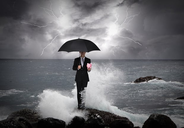 man on rocky shore in storm with umbrella