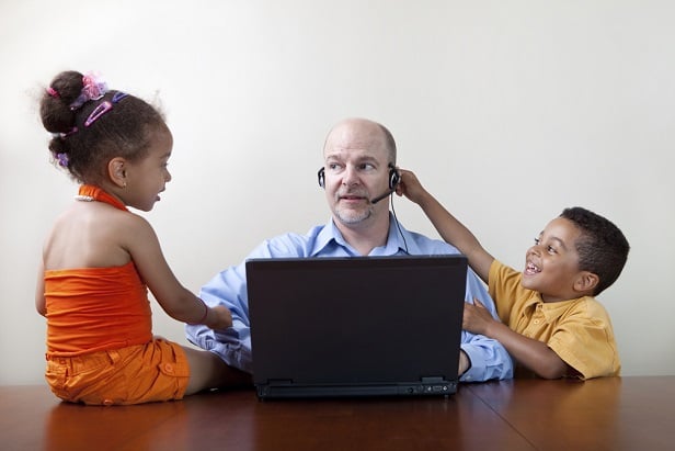 father wearing headphones at computer dealing with his two distracting children