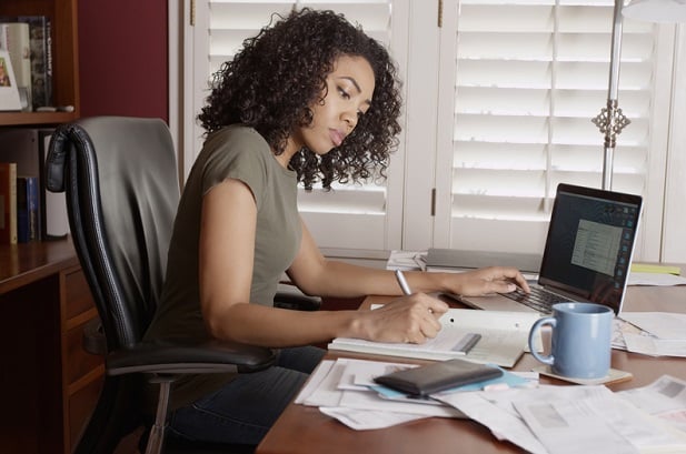 woman in home office in front of laptop writing