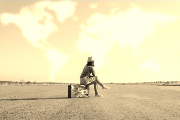 woman sitting on empty land on her suitcase waiting