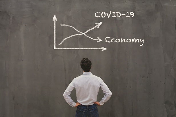 man turned to look at chalkboard with line declining for economy and line rising for covid