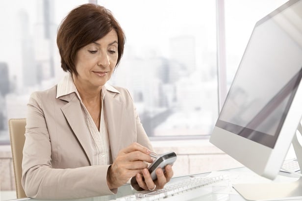 woman at computer looking at her phone
