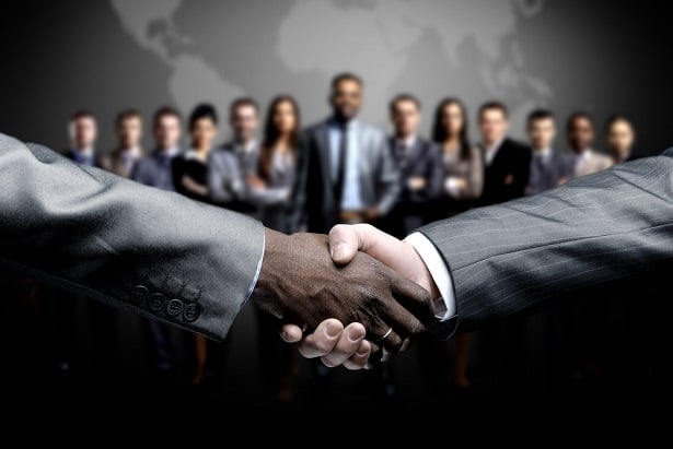 two people shaking hands in front of group of business people
