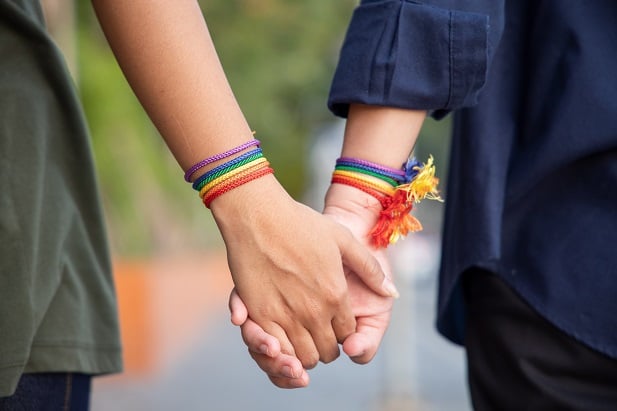 closeup of two people holding hand of LGBT women holding hands with rainbow ribbon symbol