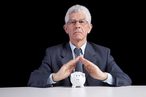 older business man with hands over piggy bank