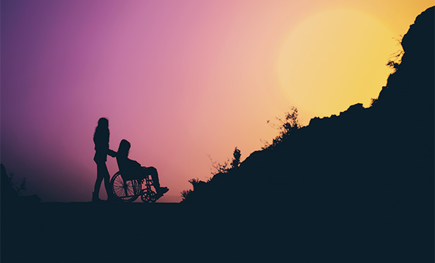 Silhouette of person pushing wheelchair up hill