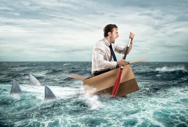 business man in tiny boat trying to row away from sharks