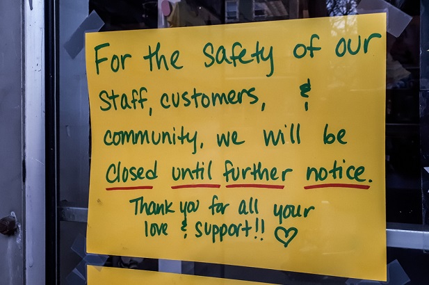 yellow handwritten sign in door saying business is closed due to covid