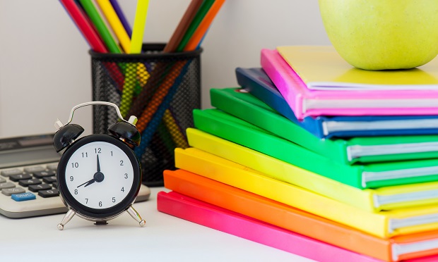Stack of rainbow colored books and alarm clock