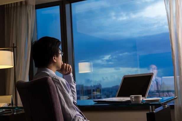 businessman at computer at window in evening staring outside and thinking