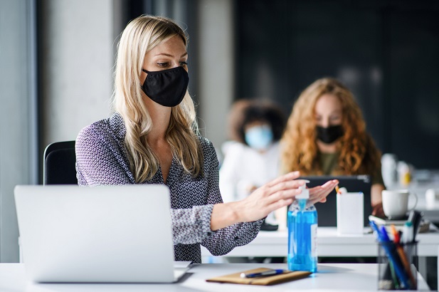 woman at office wearing mask, using hand sanitizer, socially distanced from coworker