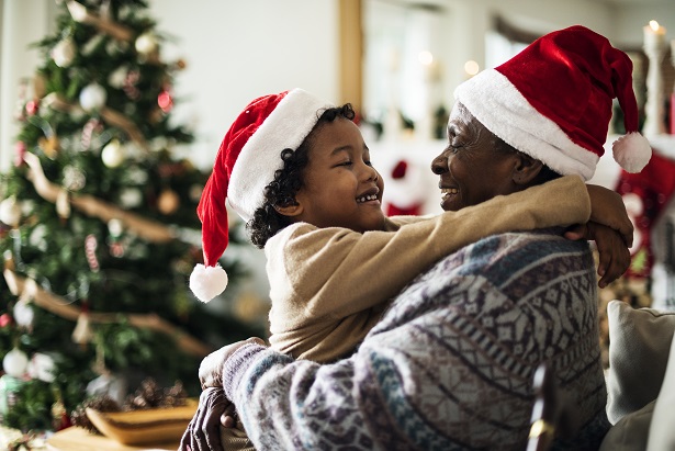 man and child in front of Christmas tree hugging and wearing Santa Claus caps