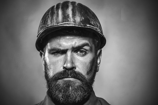 black and white photo of bearded man in hard hat with one eyebrow raised
