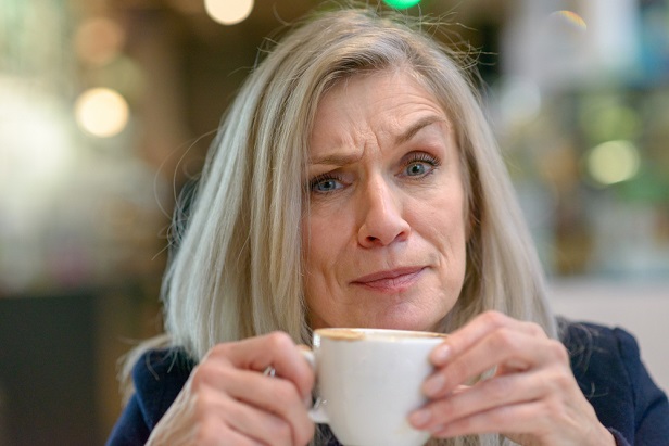 older woman holding coffee cup and raising eyebrow