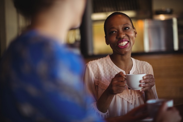 woman smiling having coffee with woman with back to camera