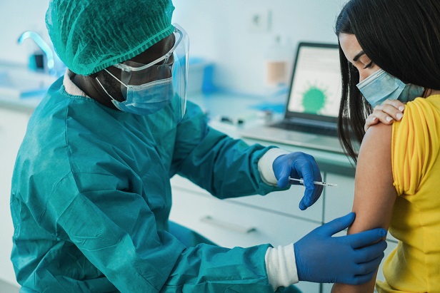 health care professional in gown and mask administering vaccine to woman