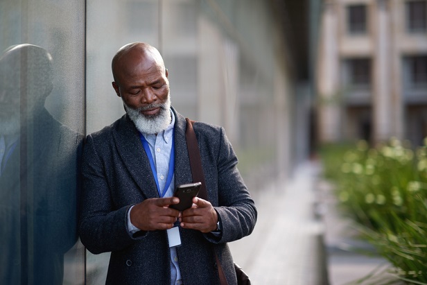 older man leaning against wall checking his smartphone