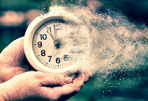 hands holding a clock dissolving into dust