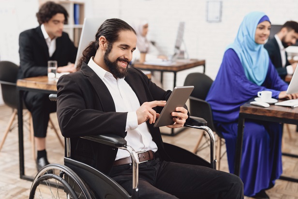 man in wheelchair using tablet in room with other employees