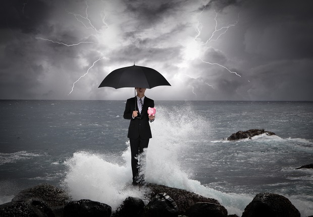 man on rock holding umbrella in storm