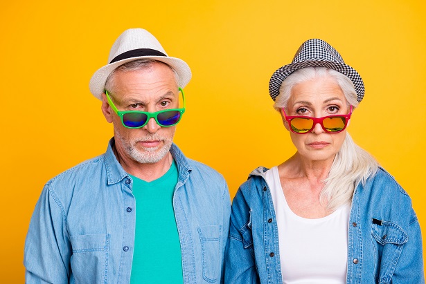 Senior couple wearing hats and eyeglasses and frowning.