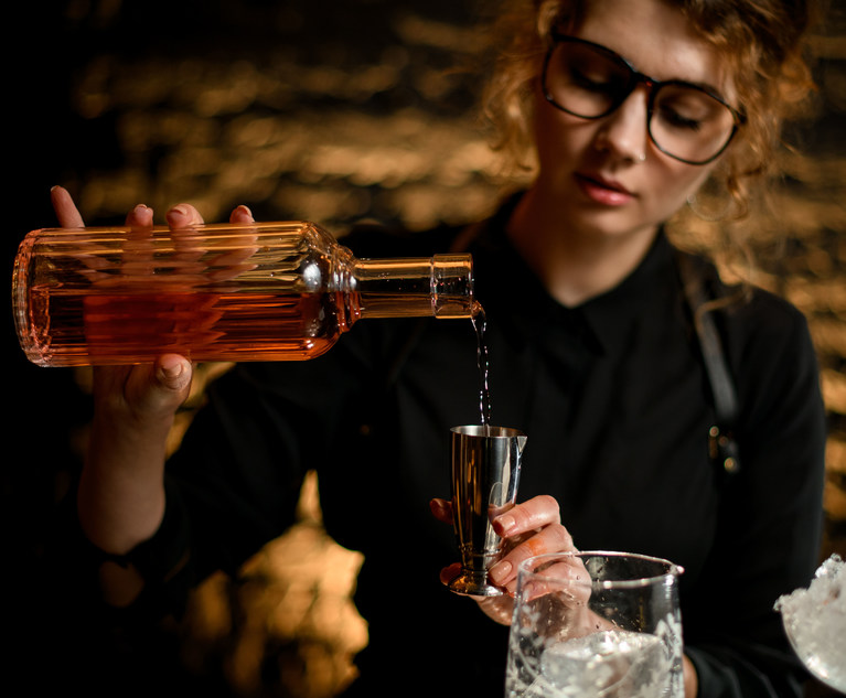 female bartender pours liquor into steel jigger.