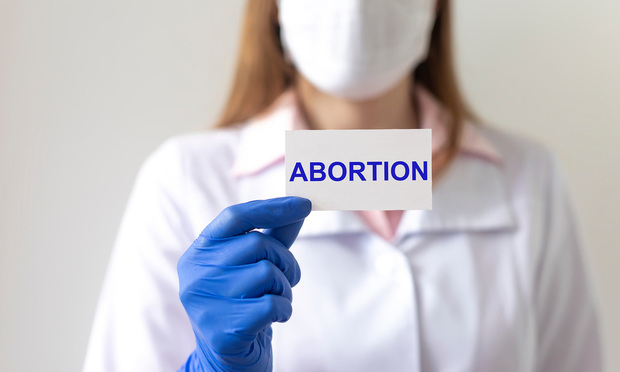 Doctor woman in protective gloves holds a paper with text abortion